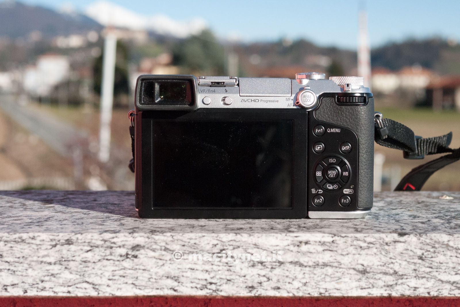 Il retro della Panasonic Lumix GX7, con lo schermo da 3 pollici touch, il mirino elettronico, la serie di bottoni per i comandi sulla destra, quattro tasti funzione personalizzabili il selettore per la messa a fuoco e l'esposizione, il pulsante per attivare il flash ed una ghiera multifunzione