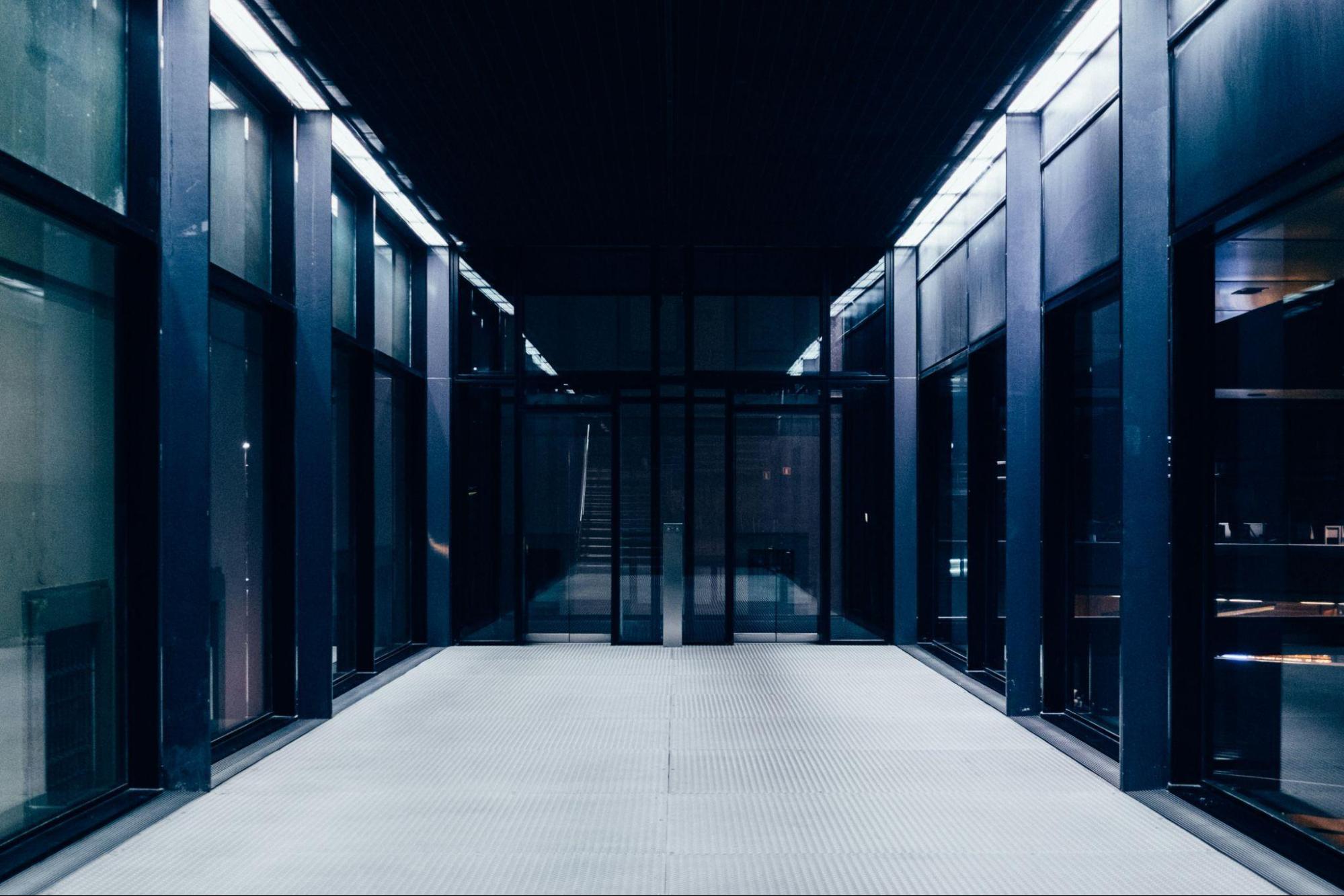 Il badge che lascia entrare il software - macitynet.it Alt text: Corridoio simmetrico di un edificio moderno con pareti vetrate e illuminazione fredda di tonalità bluastra